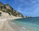 Spiaggia della Riviera del Conero con bambini che giocano e si bagnano, scogliere bianche e mare azzurro.