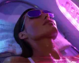 Donna con occhiali da sole si gode l'abbronzatura da lampada, illuminata da luci viola e blu.