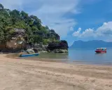 Spiaggia in Malesia con bambini su una barca rossa. Rocce verdi e mare azzurro.