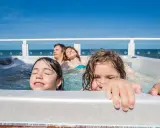 Famiglia felice in vasca idromassaggio, godendosi il Ferragosto con bambini. Il sole splende, il mare sullo sfondo.