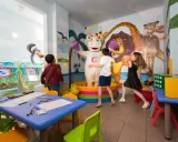 Bambini giocano con un personaggio in costume da ippopotamo in una stanza colorata, un'area giochi per famiglie al Mokambo Shore Easy Family Hotel.