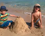 Bambini felici in vacanza in Puglia, costruiscono un castello di sabbia sulla spiaggia con il mare cristallino sullo sfondo.