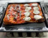 Pizza fatta in casa con pomodoro, acciughe e mozzarella appena sfornata su una teglia.