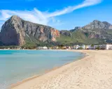 Spiaggia dorata e mare cristallino, un angolo di paradiso in Sicilia dove andare al mare. Montagne imponenti sullo sfondo.