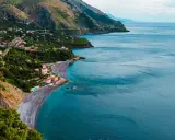 Villaggio costiero con case bianche e rosse affacciato su una spiaggia di ciottoli scuri e mare blu intenso. Le **basilicata spiagge** offrono panorami mozzafiato.