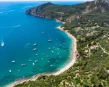 Baia incantevole con mare bello toscana, acque cristalline e barche che navigano. La costa è verdeggiante, con ville sparse tra gli alberi.