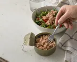Una mano prende il tonno da una scatoletta aperta per aggiungerlo a un'insalata. Quanto tonno mangiare? Una porzione sana per un pasto leggero.