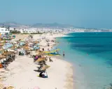 Spiaggia affollata in Marocco con bambini che giocano in acqua e famiglie che si rilassano sotto gli ombrelloni.