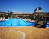 Sole e divertimento in piscina a Maiorca con bambini. Una grande struttura gonfiabile blu al centro, bagnanti e hotel sullo sfondo.