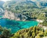 Baia verde smeraldo a Corfu, perfetta per una vacanza con bambini. Scogliere imponenti e acque cristalline invitano al gioco e all'esplorazione.