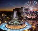 Una piazza illuminata a festa a Malta a Natale, con una fontana scintillante e una ruota panoramica che domina lo skyline al tramonto.