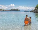 Due bambini esplorano le acque cristalline del Cilento, tra le sue spiagge perfette per famiglie. Una barca a vela all'orizzonte completa il quadro idilliaco.