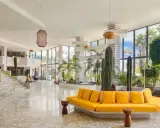 Lobby moderna con cactus e piante tropicali, divano giallo vivace e marmo lucido. Un'oasi di stile al H10 Lanzarote Princess.