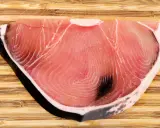 Fetta di tonnina, un pregiato pesce azzurro, su tagliere di legno. La sua carne rosa vivo mostra le tipiche striature.