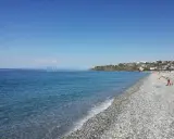 Spiaggia di ciottoli con mare azzurro e case arroccate sulla collina. Una giornata perfetta per godersi la **scalinea mare**.