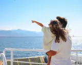 Bambina indica l'orizzonte da una nave, con la famiglia in vacanza a Favignana. Il mare azzurro e le montagne sullo sfondo creano un'atmosfera serena.