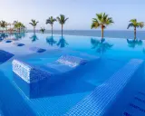 Piscina a sfioro con lettini integrati e palme, vista mare. Un sogno al searesort Riu Gran Canaria.