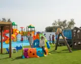 Un parco giochi colorato in una masseria per bambini in Puglia, con scivoli, tunnel e altalene. Famiglie si divertono sotto il sole.
