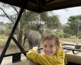 Un'avventura indimenticabile a Zanzibar con bambini: un elefante appare sullo sfondo mentre una bambina sorride dal fuoristrada.