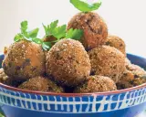 Polpette di melanzane dorate e croccanti, guarnite con prezzemolo fresco, in una ciotola blu decorata.