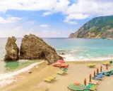 Spiagge sabbia Liguria: scogli imponenti, mare turchese e lettini pronti per il relax.