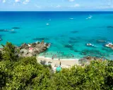 Spiaggia affollata con gente che nuota e prende il sole, barche in mare e vegetazione lussureggiante. Un angolo di paradiso del **calabria mare**.