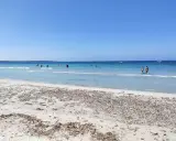 Spiaggia di Arbatax con sabbia chiara e mare cristallino, bagnanti e barche all'orizzonte. Un angolo di paradiso che ricorda la spiaggia rosa.