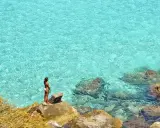 Donna su scogli ammira acque cristalline, un gioiello delle aree marine protette in Italia.