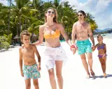Famiglia felice cammina sulla spiaggia di Mauritius con bambini, palme e mare turchese sullo sfondo.