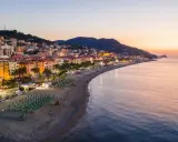 Alba sulla spiaggia finale ligure, con file di ombrelloni verdi e palme che si affacciano sul mare calmo.