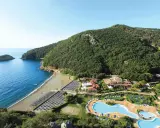 Villaggio toscana sul mare con spiaggia attrezzata, piscine e rigogliosa vegetazione che abbraccia la costa.