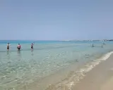 Persone in piedi nell'acqua cristallina, con la costa di Gallipoli sullo sfondo. Un perfetto giorno di mare.