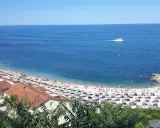 Le spiagge di Numana, con ombrelloni colorati e gente che si gode il sole, bagnate da un mare azzurro e calmo. Una barca solca l'orizzonte.