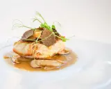 Un succulento mero pescado, guarnito con tartufo e germogli freschi, adagiato su un letto di funghi e salsa cremosa.