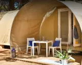 Tavolino e sedie con cuscini blu davanti a una tenda del **Gitavillage Il Gabbiano**. Lanterna blu e piante sul deck.