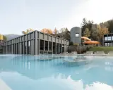 Piscina esterna con acqua fumante e scivoli acquatici arancioni al Aki Family Resort Plose. Architettura moderna in legno e montagne sullo sfondo.