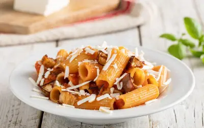 Un piatto invitante di pasta alla norma con melanzane fritte, pomodoro e ricotta salata grattugiata, pronto per essere gustato.