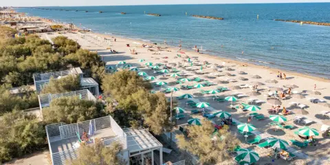 Lidi ferraresi: una distesa di ombrelloni verdi e bianchi sulla sabbia dorata, con il mare azzurro e alcune persone che si godono il sole.