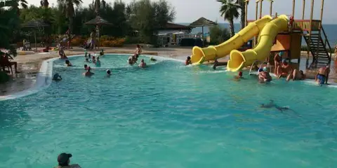 Piscina con scivoli gialli e persone che nuotano, ideale per campeggi puglia sul mare per bambini.
