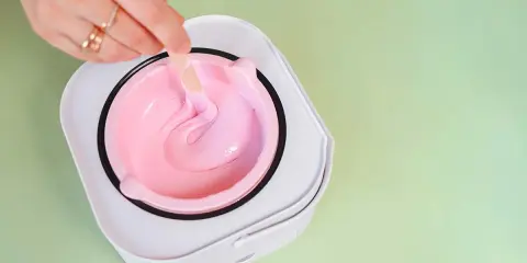 Mano con anelli mescola cera rosa in un scaldacera. Preparazione per la ceretta prima del mare.