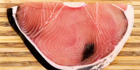 Fetta di tonnina, un pregiato pesce azzurro, su tagliere di legno. La sua carne rosa vivo mostra le tipiche striature.
