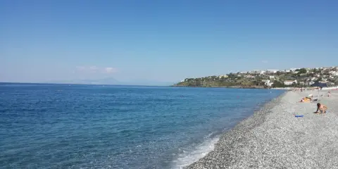 Spiaggia di ciottoli con mare azzurro e case arroccate sulla collina. Una giornata perfetta per godersi la **scalinea mare**.