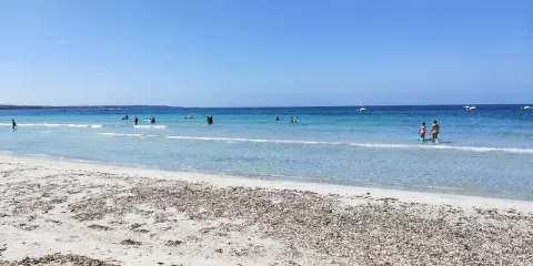 Spiaggia di Arbatax con sabbia chiara e mare cristallino, bagnanti e barche all'orizzonte. Un angolo di paradiso che ricorda la spiaggia rosa.