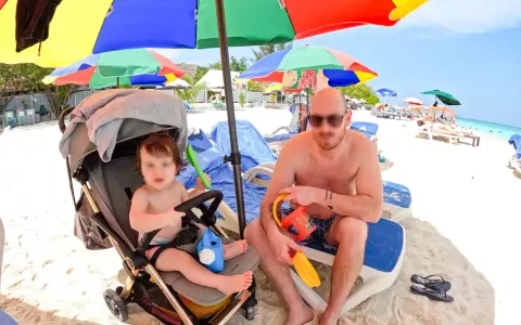 Un papà e il suo bambino si godono una giornata di sole alle Maldive con bambini, tra giochi sulla sabbia e relax sotto gli ombrelloni colorati.