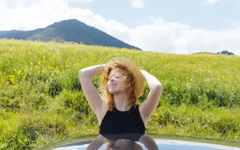 Ragazza con cappello di paglia al sole, godendosi la natura. Un modo per pensare a come abbronzarsi velocemente il viso in estate.