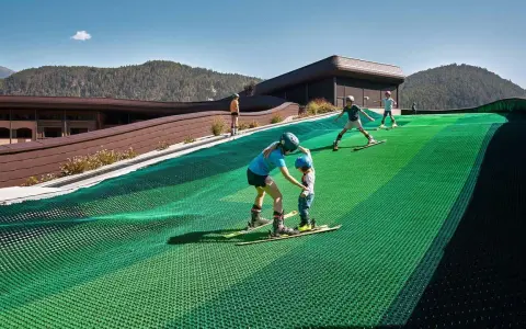 Bambini imparano a sciare su una pista verde al Falkensteiner Family Resort Lido, con montagne sullo sfondo.