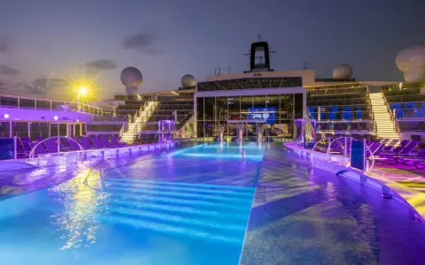 Piscine illuminate con luci viola e blu sulla MSC World Europa, con sdraio e scale illuminate.