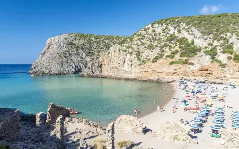 Spiaggia affollata con ombrelloni colorati, acque cristalline e scogliere verdi. Perfetta per vacanze al mare economiche e rilassanti.