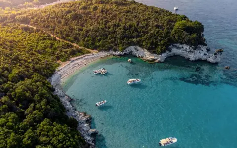 Baia con acque cristalline e vegetazione lussureggiante, ideale per famiglie. Diverse barche ormeggiate, perfette per esplorare le isole greche.