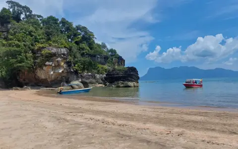 Spiaggia in Malesia con bambini su una barca rossa. Rocce verdi e mare azzurro.
